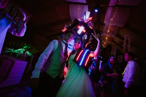 Hombre y mujer posan junto a una persona con un traje iluminado detrás de ellos.