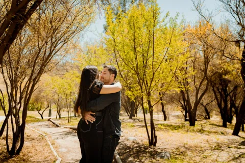 Hombre y mujer se besan bajo árboles con follaje amarillo.