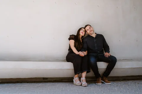Hombre y mujer están sentados juntos en una banca integrada a un muro curvo claro.
