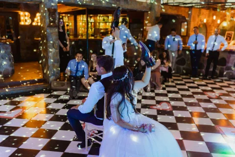 Hombre y mujer sentados espalda con espalda levantan distintos zapatos frente a un grupo de personas.