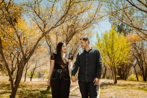 Hombre y mujer permanecen tomados de la mano sobre un sendero entre árboles.