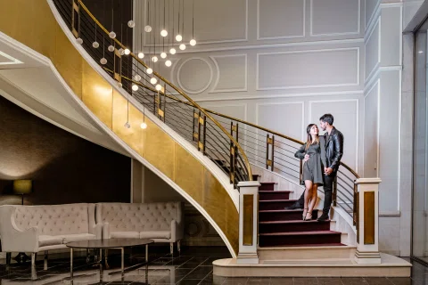 Hombre y mujer vestidos con tonos oscuros posan juntos en una escalera interior.