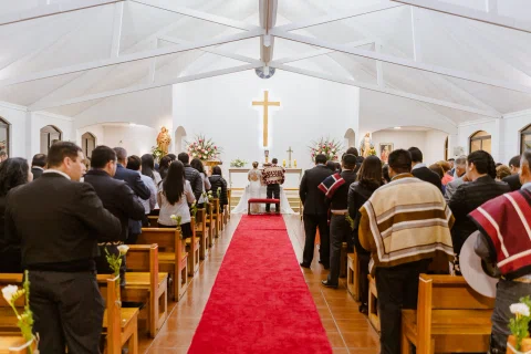 Vista central de una iglesia con un pasillo rojo y numerosas personas a ambos lados.