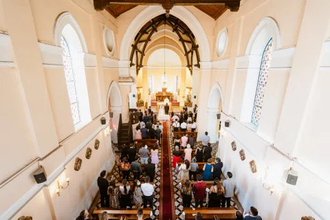 Vista elevada del interior de una iglesia con un pasillo rojo y numerosas personas sentadas.