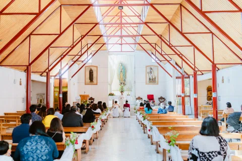 Interior de la iglesia visto desde el fondo con la estructura roja del techo visible.