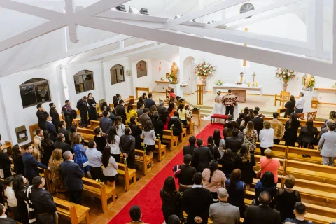 Vista elevada del interior de una iglesia con numerosas personas de pie a ambos lados del pasillo.