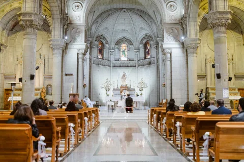 Interior de una iglesia con bancas ocupadas y el altar al fondo.
