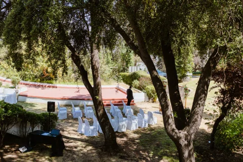 Espacio de ceremonia en un jardín visto entre troncos y ramas de árboles.