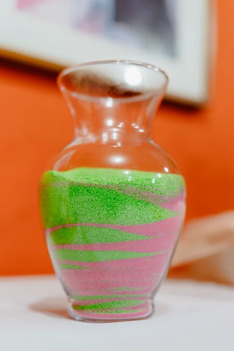 Jarra de vidrio con capas onduladas de material granular verde y rosado.