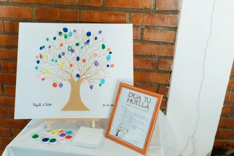 Lámina de árbol con huellas de colores, almohadillas de tinta y un cartel sobre una mesa.