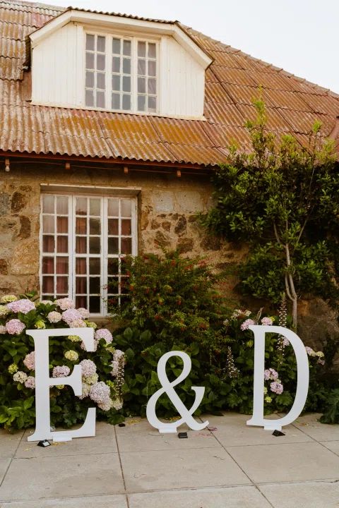 Letras decorativas con iniciales dispuestas frente a una casa de la celebración.