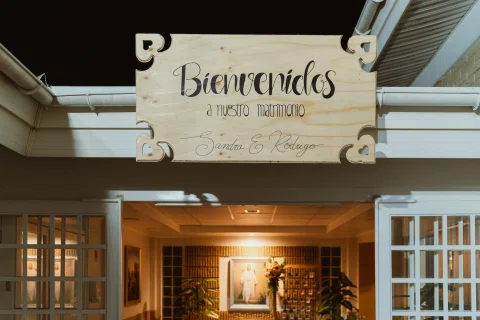 Letrero de madera con el texto «Bienvenidos a nuestro matrimonio» sobre una entrada decorada.