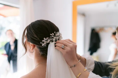 Mano coloca un accesorio floral en el peinado recogido de una mujer.