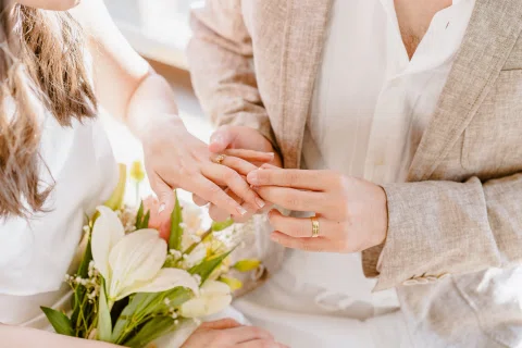 Detalle de una mano mostrando un anillo junto a flores claras.