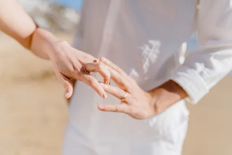 Detalle de una mano mostrando un anillo con ropa blanca alrededor.