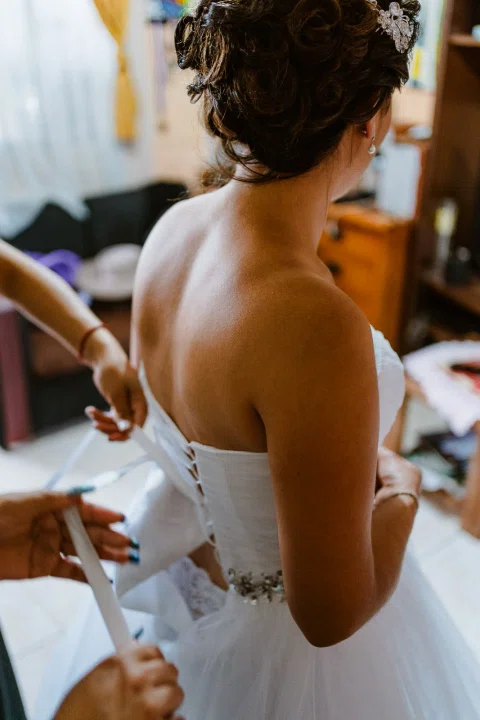 Dos manos ajustan la espalda de un vestido blanco mientras la mujer permanece de espaldas.