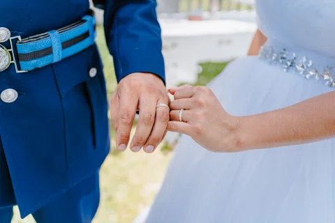 Detalle de las manos con anillos junto al uniforme azul y el vestido blanco.