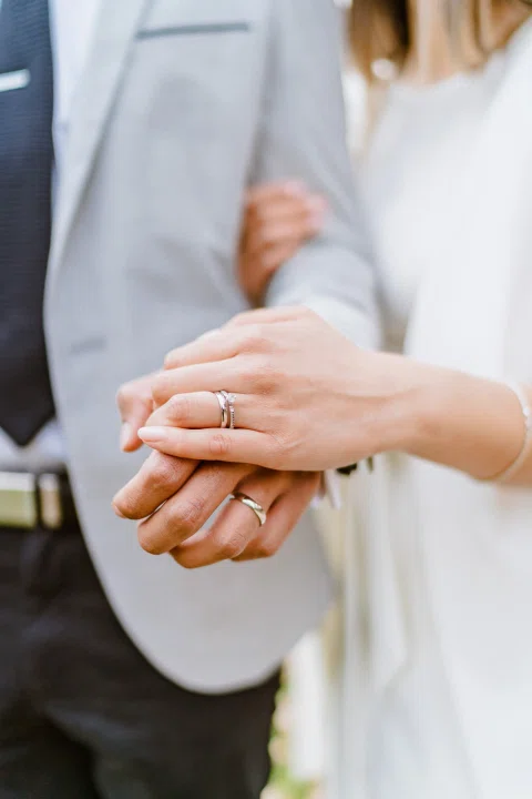 Detalle de las manos con anillos junto a la manga de un traje claro.