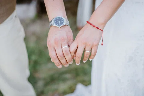 Detalle de las manos de un hombre y una mujer juntas, con anillos visibles y un reloj de pulsera.