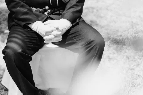 Detalle en blanco y negro de las manos de un hombre con uniforme apoyadas sobre sus piernas.