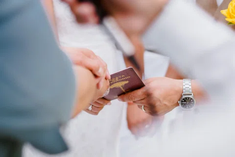 Manos sostienen una libreta de matrimonio; también se ven anillos y un reloj de pulsera.