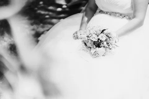 Detalle en blanco y negro de las manos de una mujer sosteniendo un ramo sobre el vestido.