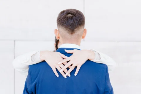 Detalle de las manos de una mujer apoyadas sobre la espalda de un hombre con traje azul.