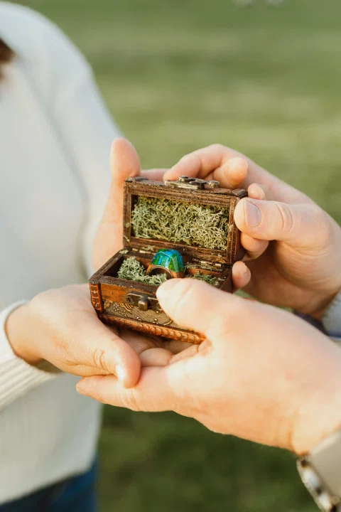 Manos sosteniendo una pequeña caja abierta con un anillo en su interior.