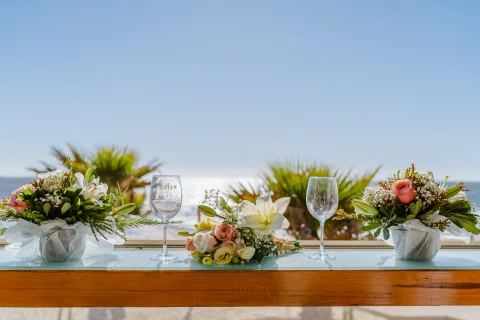Mesa decorada con flores y copas frente a una amplia vista al mar.