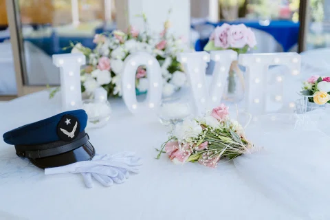 Mesa decorada con flores, copas y una gorra de uniforme azul.