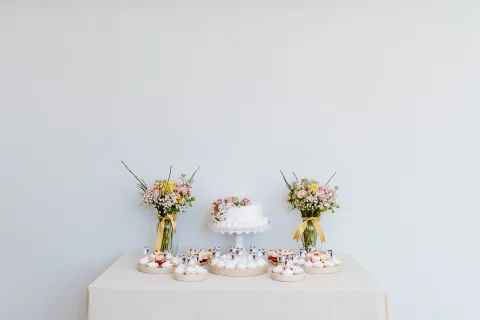 Mesa de postres con torta y arreglos florales sobre un fondo claro.