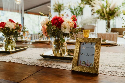 Mesa principal decorada con flores rojas y rosadas junto a un cartel enmarcado que dice “Los Joya”.