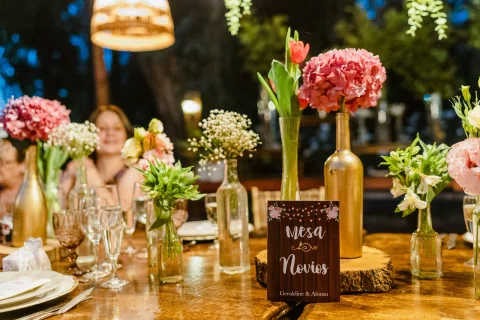 Mesa de recepción decorada con flores rosadas, botellas y pequeños carteles.