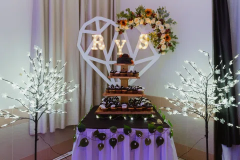 Mesa de torta decorada con iniciales, flores y luces blancas.