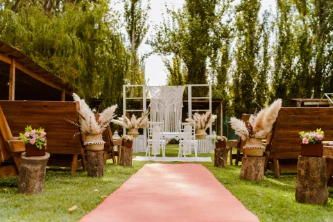 Montaje de ceremonia exterior con alfombra roja, sillas blancas y arreglos de pampas a ambos lados.