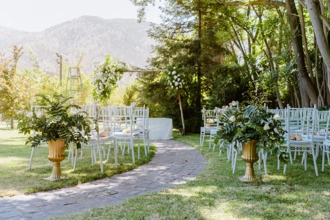 Montaje de ceremonia en jardín con sillas blancas y un sendero curvo.