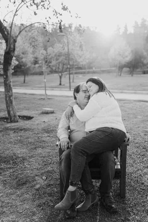Mujer abraza a un hombre sentado en una silla, en una fotografía en blanco y negro.