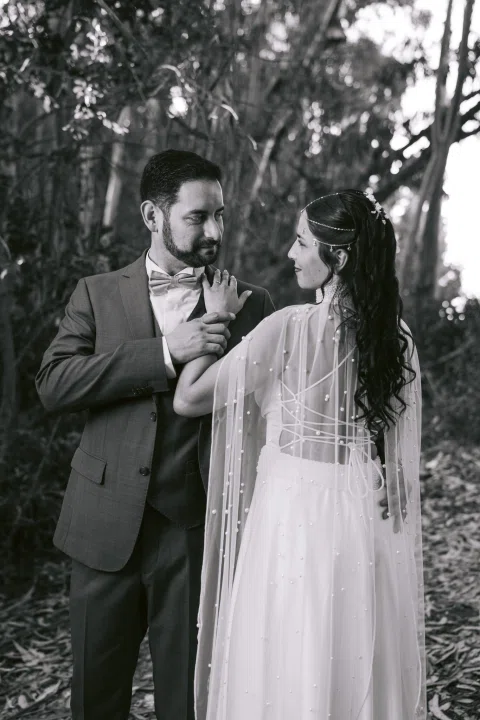 Mujer con vestido blanco acomoda el corbatín de un hombre con traje, en una fotografía en blanco y negro.