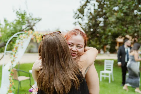 Mujer de cabello rojo abraza a una mujer de cabello largo sobre el césped.