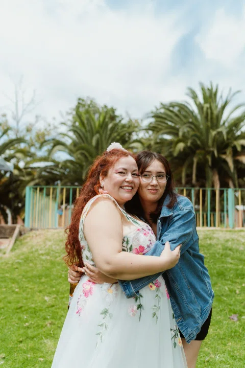 Mujer de cabello rojo abraza a una mujer con chaqueta azul sobre el césped.