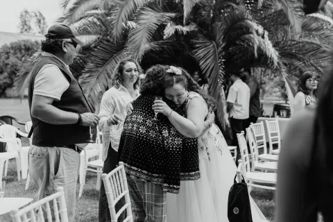 Mujer de cabello rojo abraza a una mujer con blusa estampada, en una fotografía en blanco y negro.