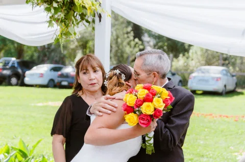 Mujer con un ramo de flores abrazando a un hombre mayor al aire libre.
