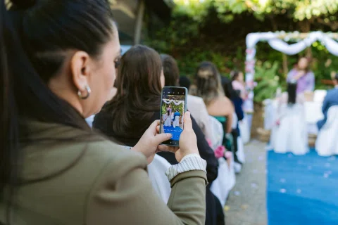 Mujer sostiene un teléfono para fotografiar una escena junto a un arco floral.