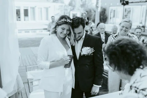 Mujer vestida de blanco y hombre con traje oscuro aparecen juntos en una fotografía en blanco y negro al aire libre.
