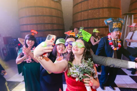Mujer con lentes verdes sostiene un celular para una fotografía grupal mientras otras personas usan accesorios de fiesta.