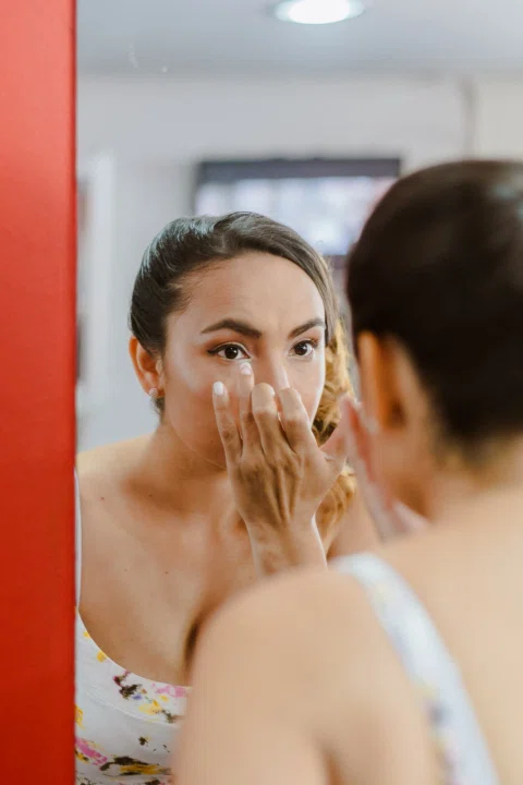 Mujer aplicándose maquillaje frente a un espejo durante los preparativos.