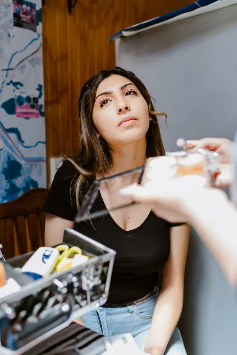 Mujer sentada mira hacia arriba mientras recibe maquillaje alrededor de los ojos.