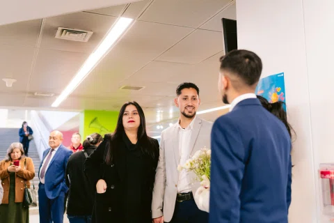 Mujer vestida de negro y hombre con chaqueta clara permanecen frente a un hombre con traje azul visto de espaldas.
