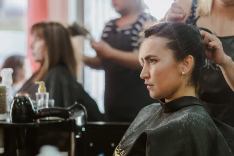 Mujer sentada mientras una persona arregla su cabello durante los preparativos.