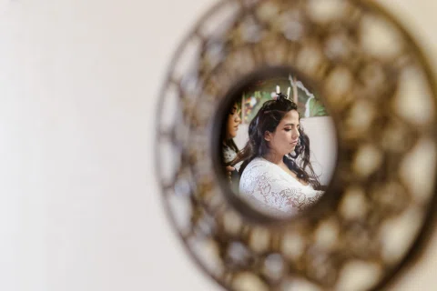 Mujer con prenda blanca reflejada en un pequeño espejo decorativo dentro de una habitación.